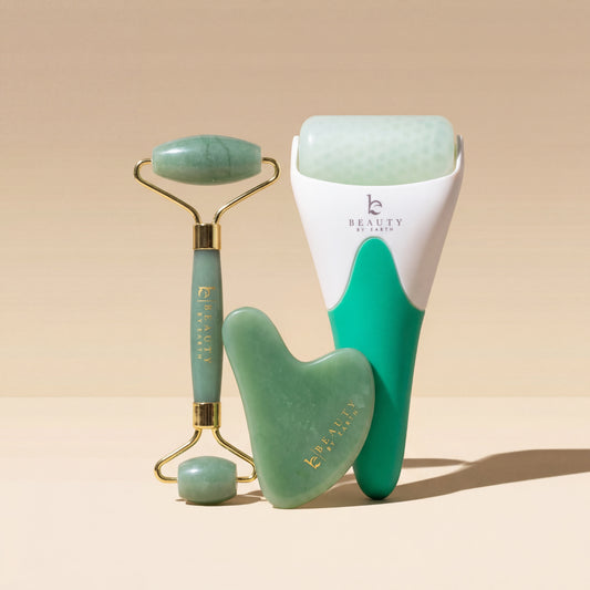 Set of jade tools including a roller, gua sha tool, and face roller on a beige background.