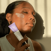 Woman applying skincare product to her face with a tube of cream.