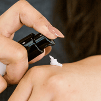 Person applying cream to their leg with a black bottle.