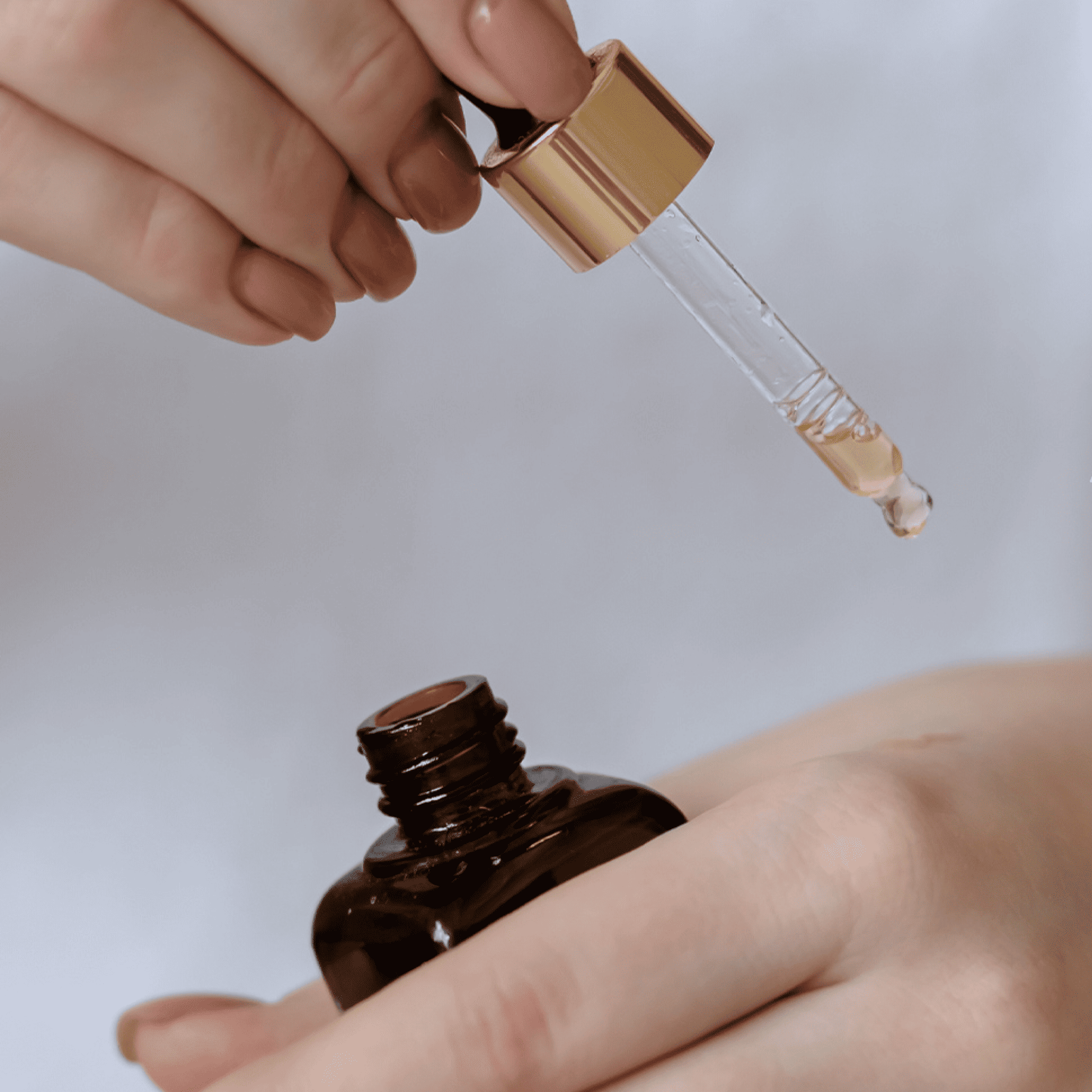 Hand holding a dropper with a brown bottle against a light background