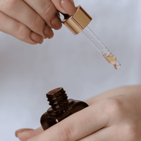 Hand holding a dropper with a brown bottle against a light background