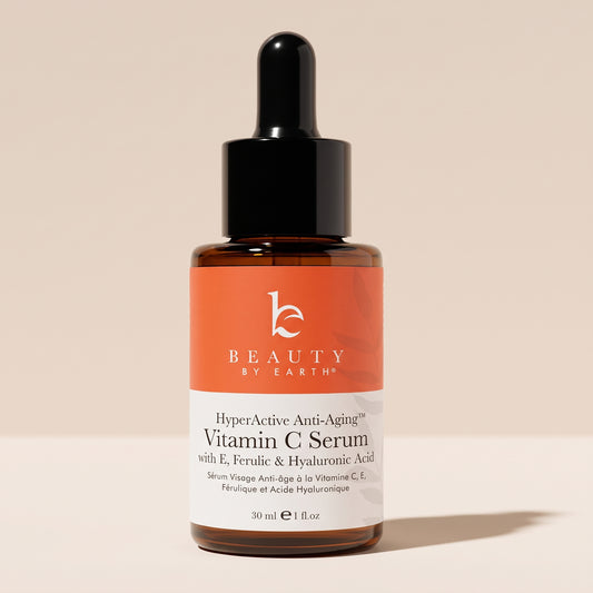 Beauty by Earth HyperActive Anti-Aging Vitamin C Serum in an amber glass dropper bottle with an orange and white label, against a soft beige background.