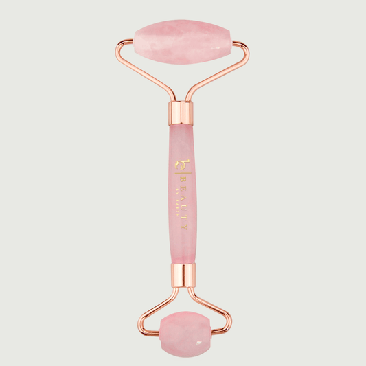 Pink and rose gold facial roller on a light gray background