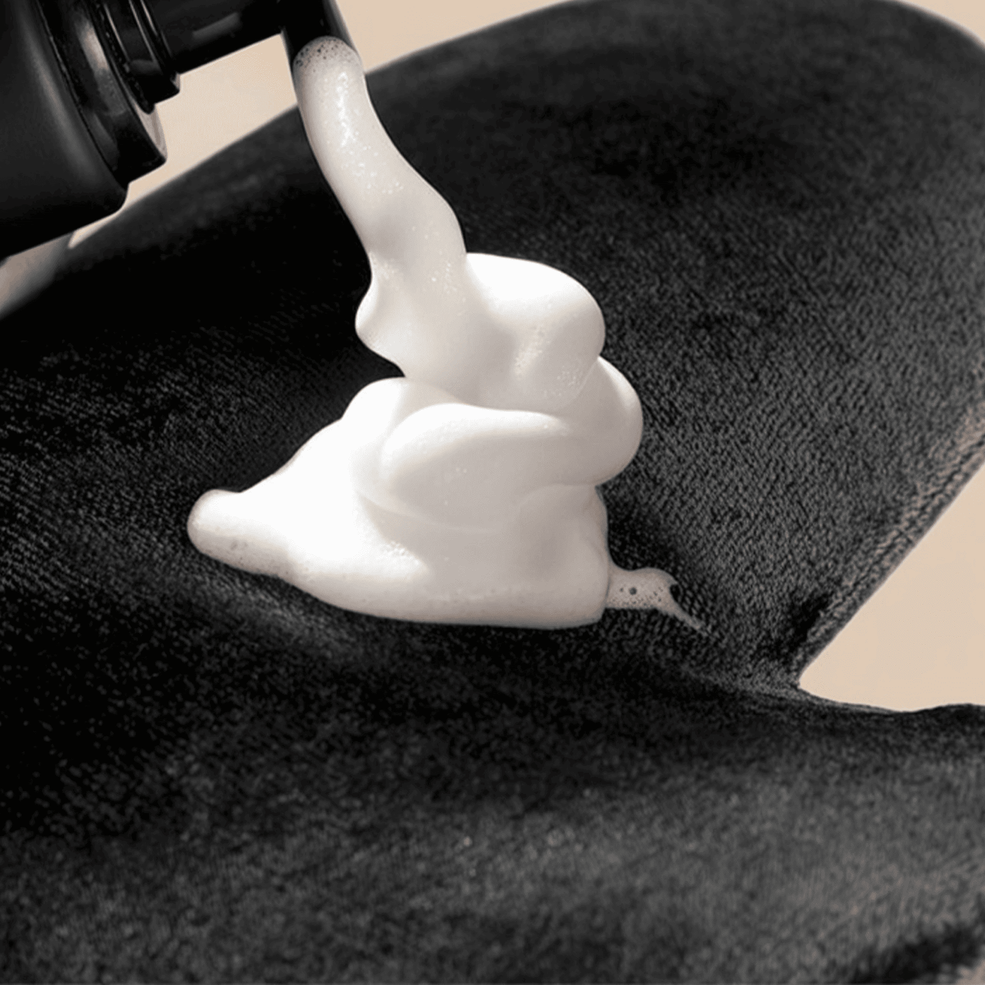 Self Tanner mousse being applied to a black towel with a close-up view.
