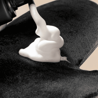 Self Tanner mousse being applied to a black towel with a close-up view.