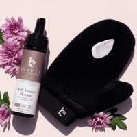 Beauty by Earthmott Self Tanner Mousse bottle with black mitt and pink flowers on a light pink background