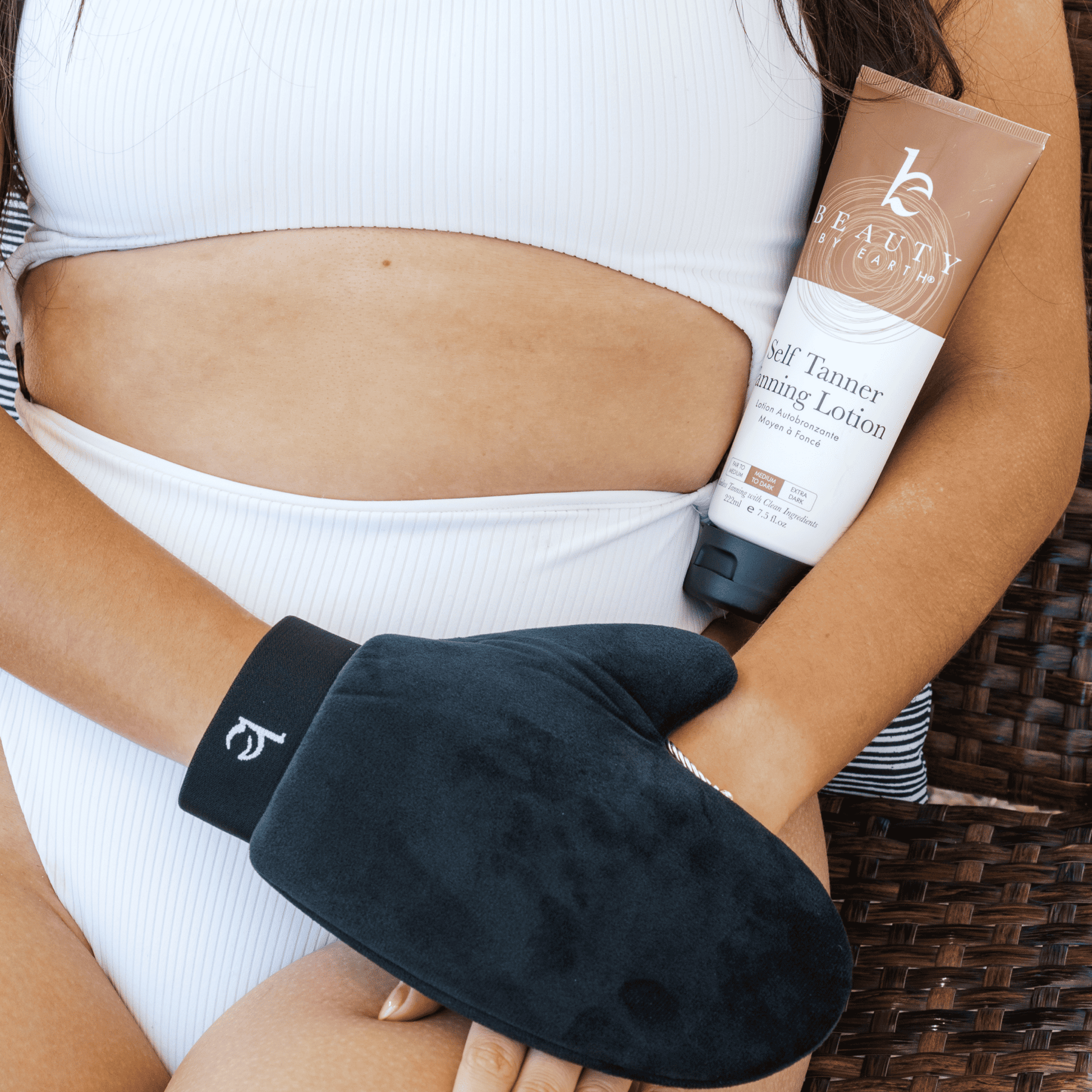 Model holding self tanner tanning lotion medium to dark and body applicator mitt on hand