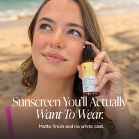 A woman on a beach holds a bottle of Sunscreen Serum. The image features a dark overlay with the text 'Sunscreen You'll Actually Want To Wear.