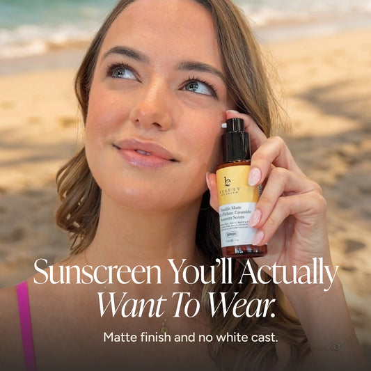 A woman on a beach holds a bottle of Sunscreen Serum. The image features a dark overlay with the text 'Sunscreen You'll Actually Want To Wear.