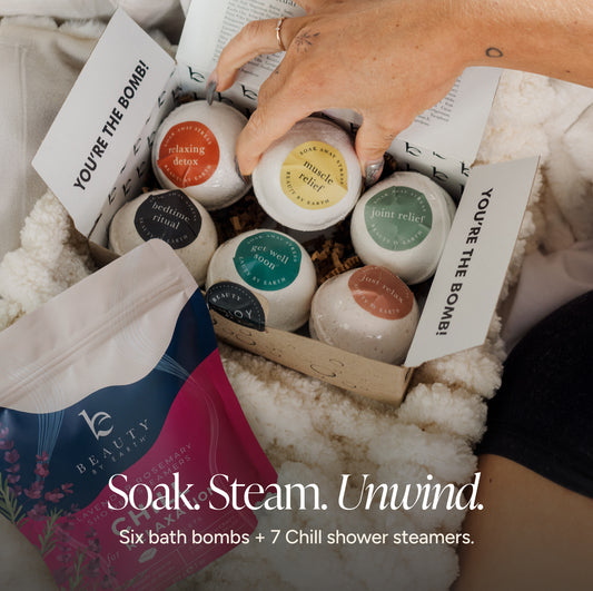 Beauty by Earth Bath Bomb Gift Set featuring six bath bombs in an open box, paired with Lavender Rosemary Chill Shower Steamers. A hand reaches for a bath bomb, with the text “Soak. Steam. Unwind.” overlaid.
