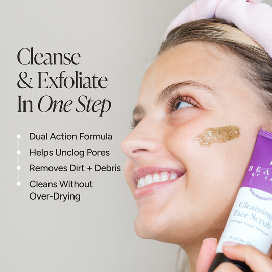 A smiling woman with a pink headband applies a brown exfoliating face scrub to her cheek while holding a purple and white tube labeled face scrub. Text on the left reads 'Cleanse & Exfoliate In One Step' with bullet points about the dual action formula.