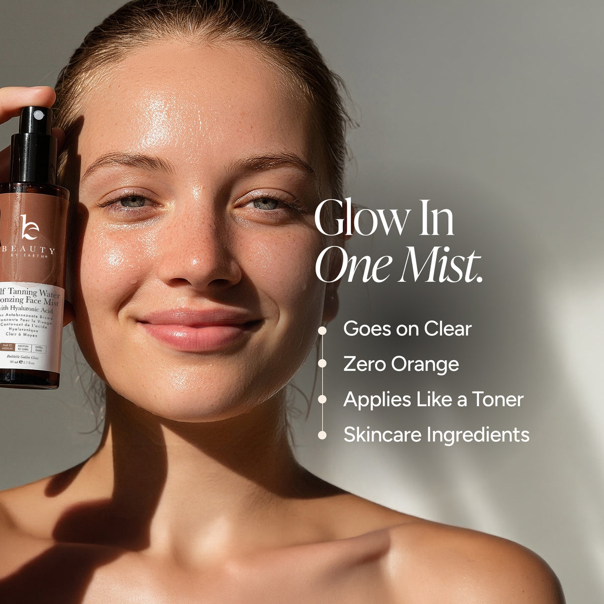 A woman with dewy skin holds a bottle of bronzing Face Mist next to her face. The image features text overlays reading 'Glow In One Mist.