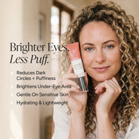 A woman with curly blonde hair holds a tube of eye cream next to text describing its benefits: 'Brighter Eyes, Less Puff.' The tube is peach and white with a black cap, and the background is a softly blurred indoor setting.