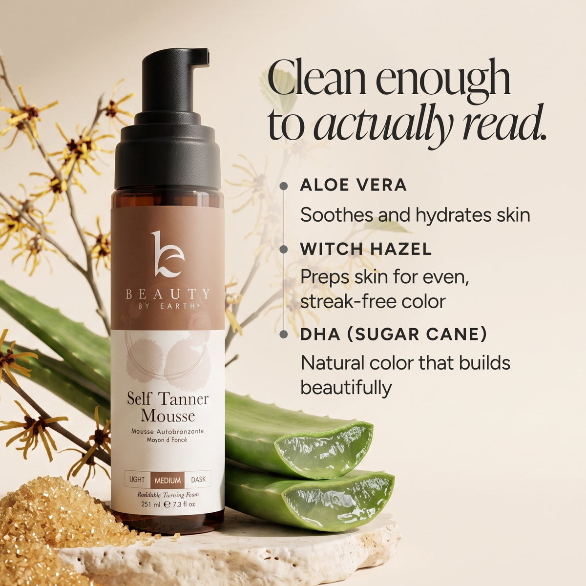 A bottle of Beauty by Earths Self Tanner Mousse displayed on a stone slab with aloe vera leaves and sand. The background is a warm beige with text detailing the ingredients (Aloe Vera, Witch Hazel, DHA (Sugarcane)) and a tagline 'Clean enough to actually read.