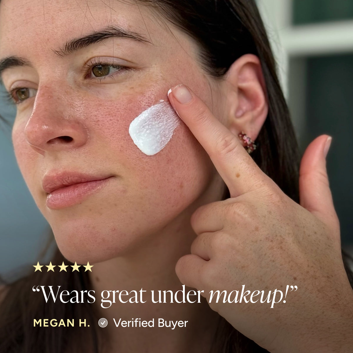 Close-up of a woman applying sunscreen serum to her cheek, with text overlay reading 'Wears great under makeup!' and 'MEGAN H. Verified Buyer'.