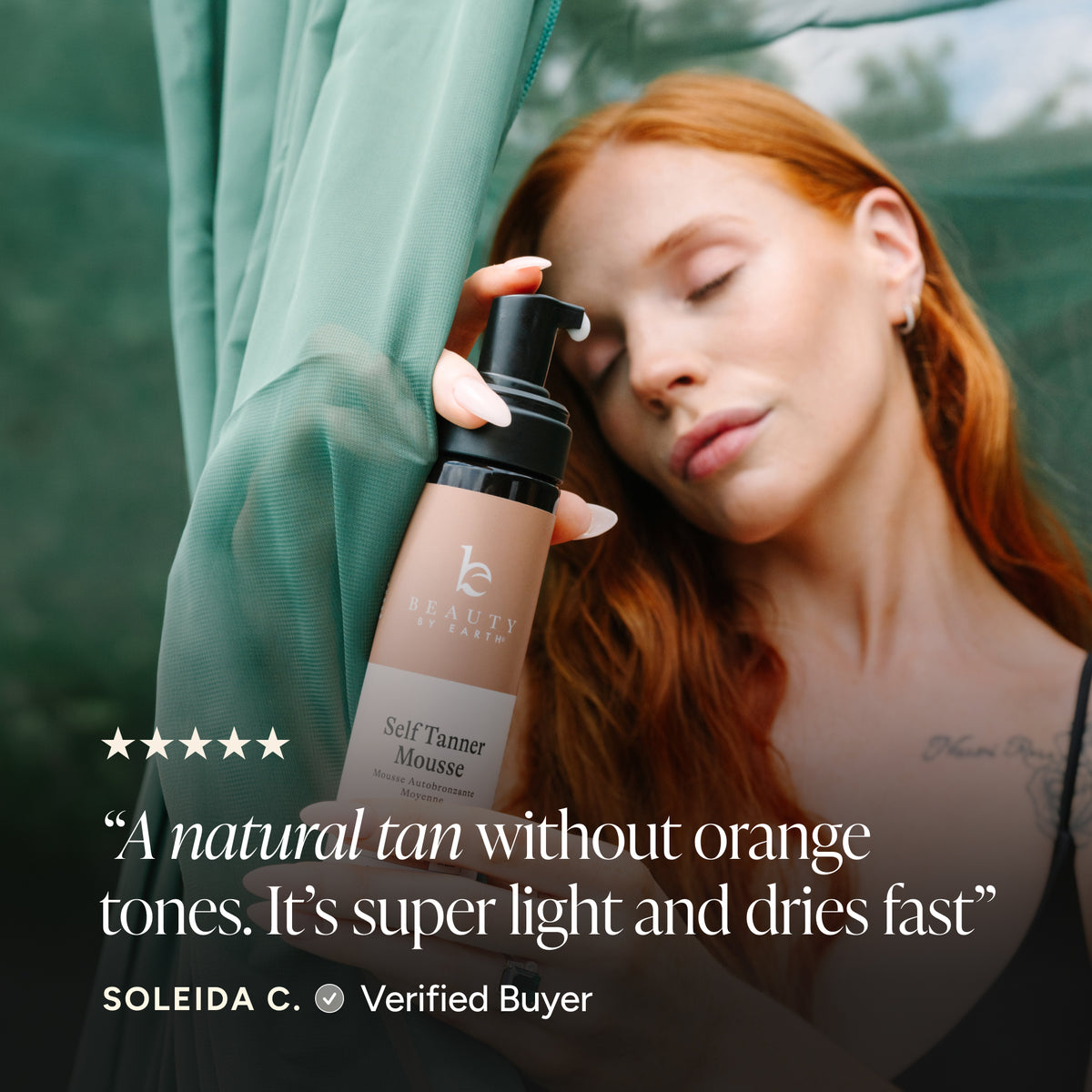 A woman with red hair rests against a sheer teal curtain while holding a bottle of Self Tanner Mousse. The image includes a five-star rating graphic and a customer quote overlay on a dark green background.
