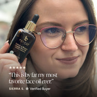 A close-up lifestyle shot of a woman holding a bottle of Beauty of Earth Face Oil next to her face. The image features a five-star rating graphic and a verified buyer badge with the text, 'This is by far my most favorite face oil ever.