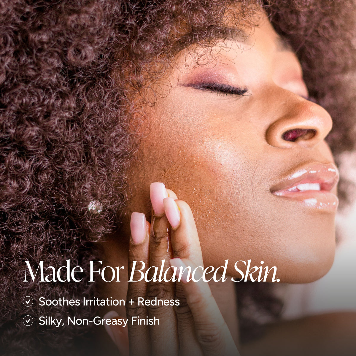 Close-up of a woman with curly hair touching her cheek, with text reading 'Made For Balanced Skin. Soothes Irritation + Redness' and 'Silky, Non-Creasy Finish.
