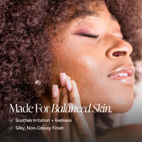Close-up of a woman with curly hair touching her cheek, with text reading 'Made For Balanced Skin. Soothes Irritation + Redness' and 'Silky, Non-Creasy Finish.