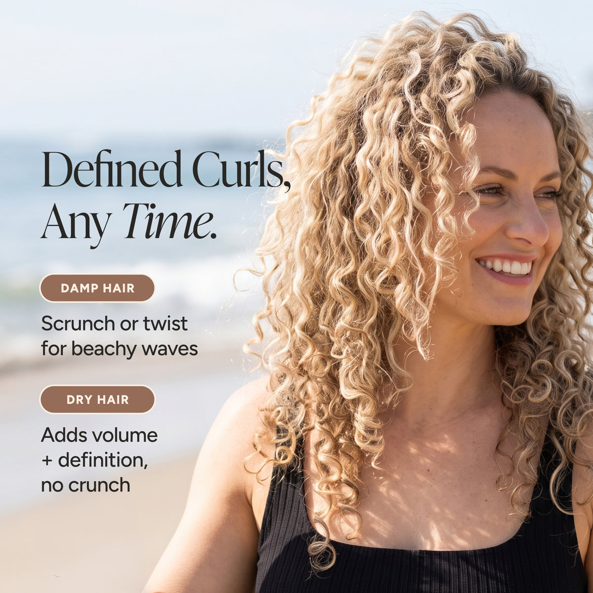 A smiling woman with long, defined curly blonde hair stands outdoors near the beach, wearing a black ribbed top. Text on the left reads, 'Defined Curls, Any Time.