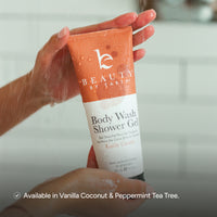 A person holds a tube of Beauty by Earth Body Wash Shower Gel under running water. The tube is orange and white with the brand logo and product name clearly visible.