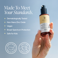A hand holds a bottle of Beauty by Earth Barrier Defense Cellular Sunscreen against a soft blue sky background, with marketing text and certification badges on the left.