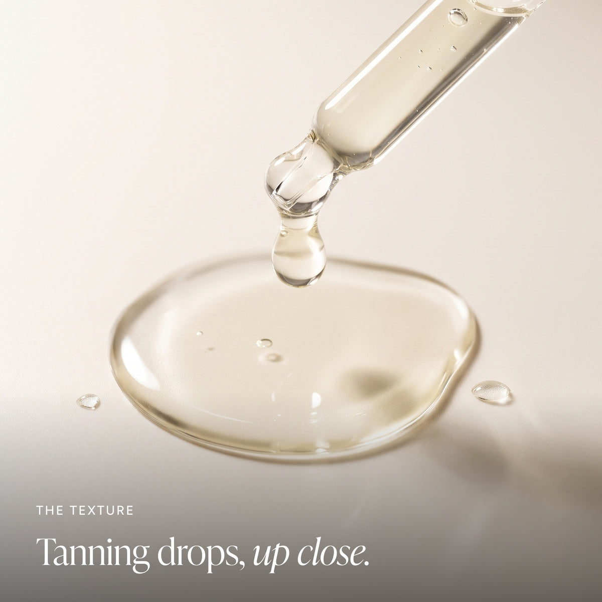 A close-up of a clear glass dropper releasing tanner drops into a smooth surface, with the text 'THE TEXTURE Tanning drops, up close.' in the lower left.