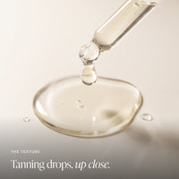 A close-up of a clear glass dropper releasing tanner drops into a smooth surface, with the text 'THE TEXTURE Tanning drops, up close.' in the lower left.