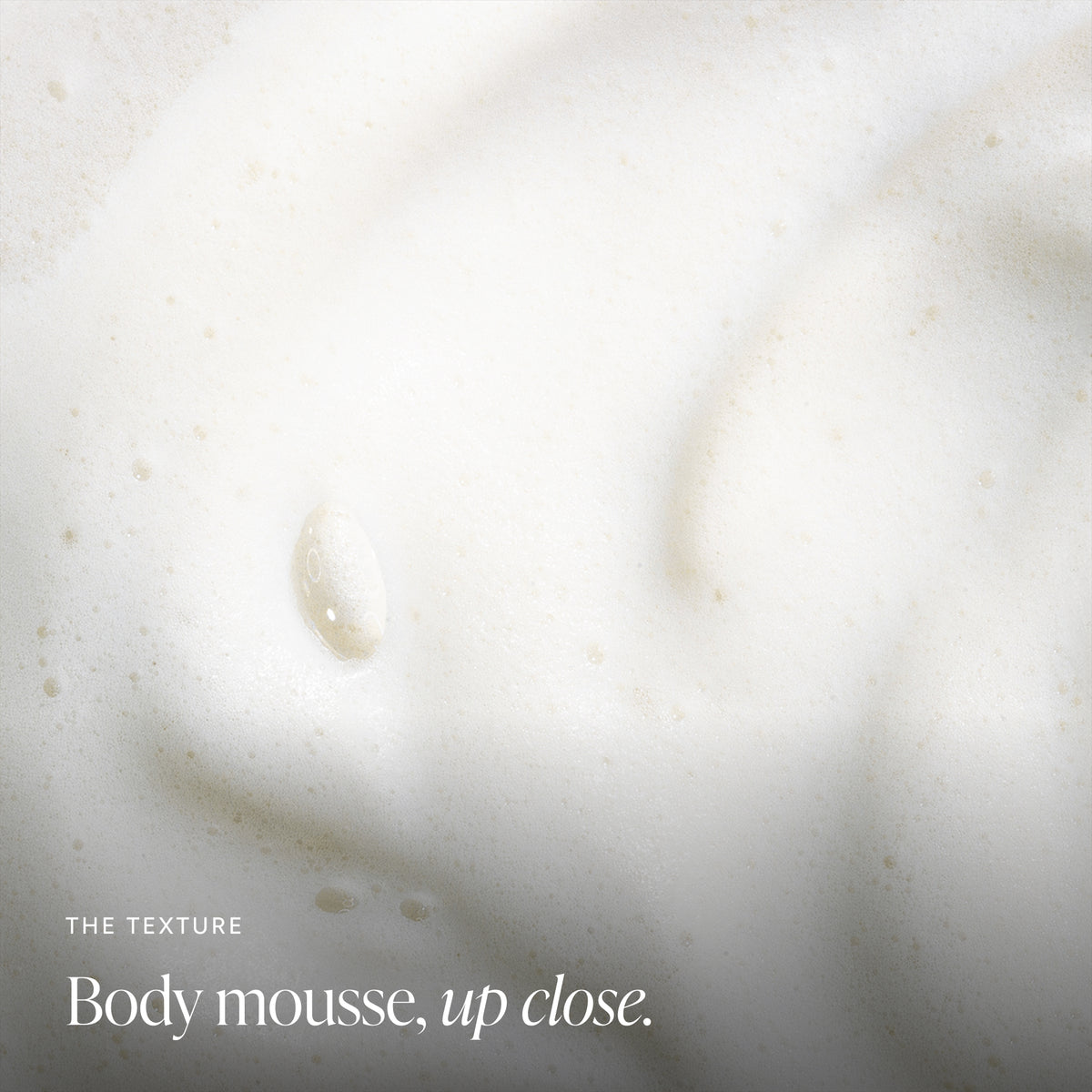 Close-up of white body mousse with small bubbles and the text 'THE TEXTURE Body mousse, up close.'