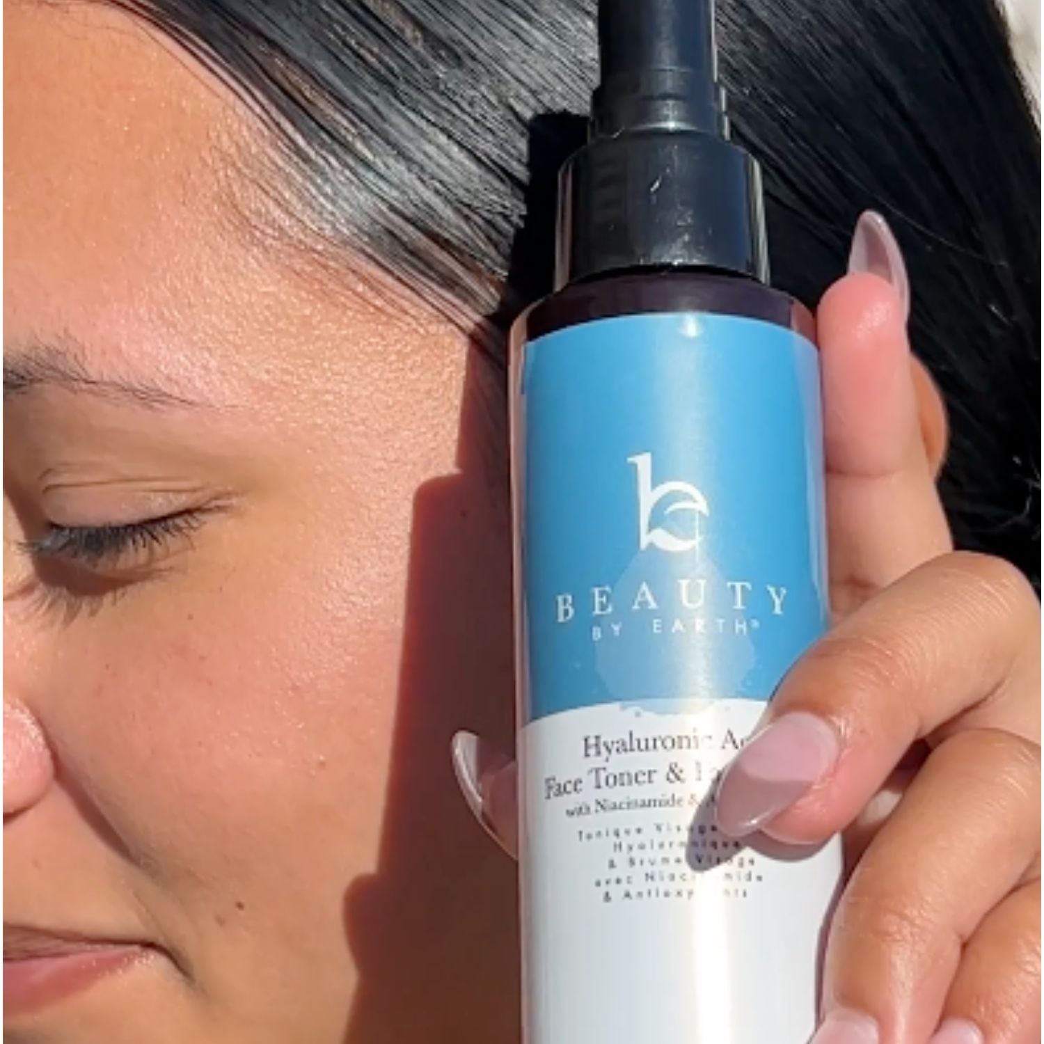 Person holding a bottle of 'Beauty by Earthly' skincare product close to their face.