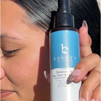 Person holding a bottle of 'Beauty by Earthly' skincare product close to their face.