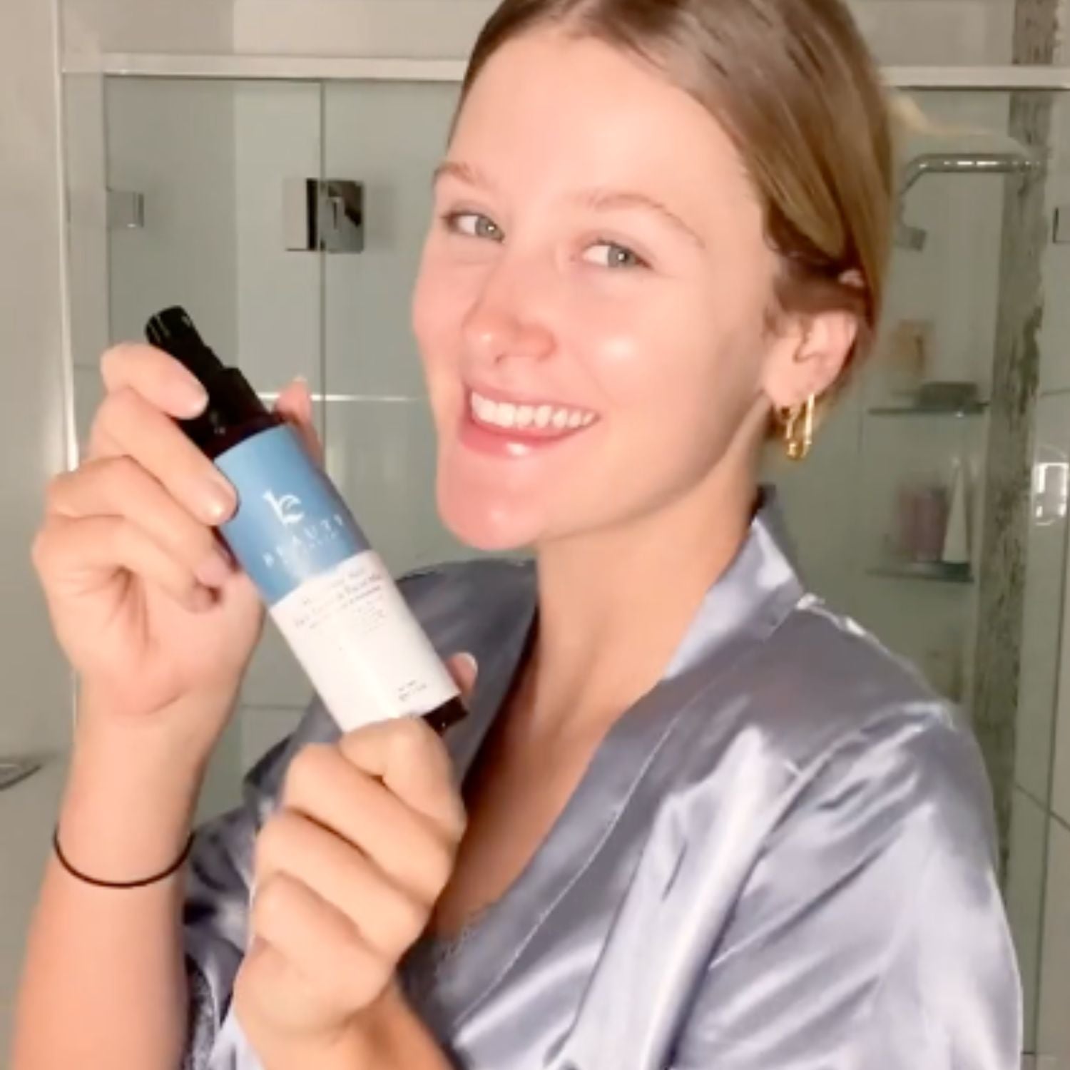 Woman holding a bottle of skincare product in a bathroom setting
