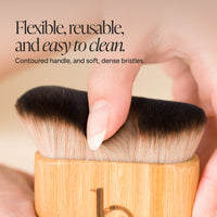 A close-up of a blending brush with a contoured bamboo handle and dark brown to beige bristles, held in hands with promotional text overlay.