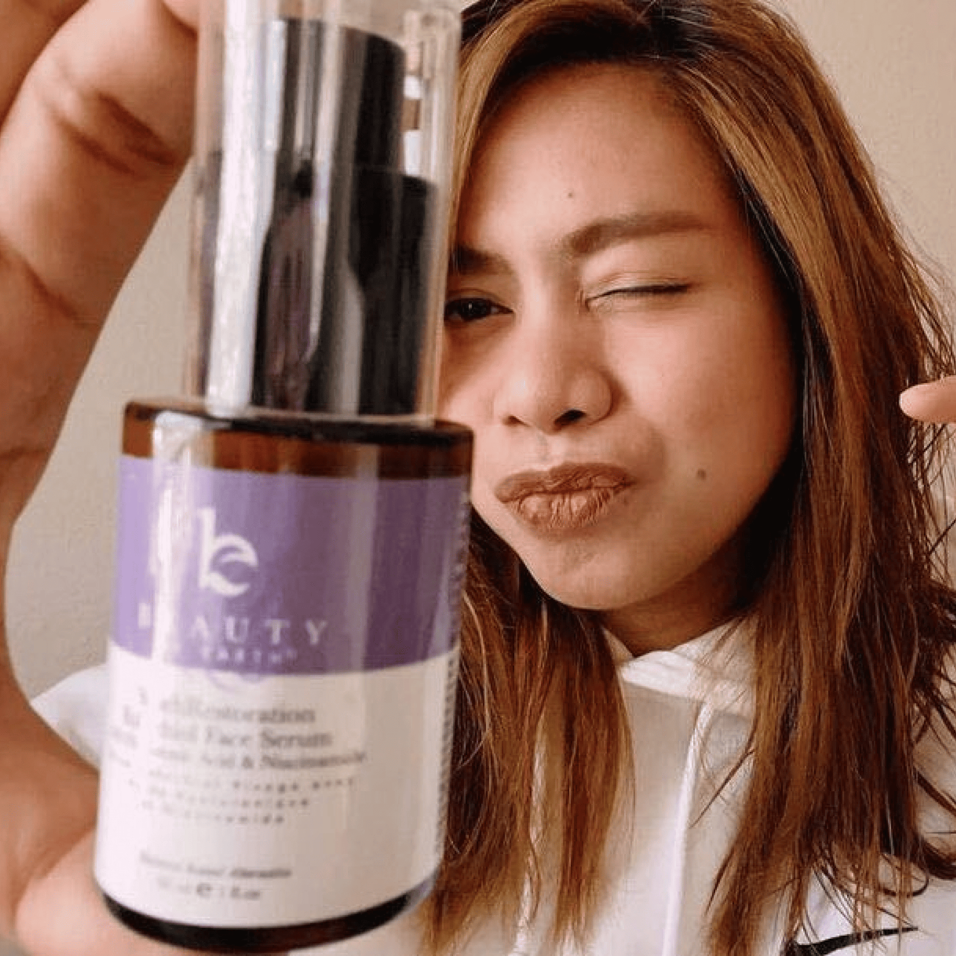 Person holding a bottle of 'The Beauty' serum close to their face