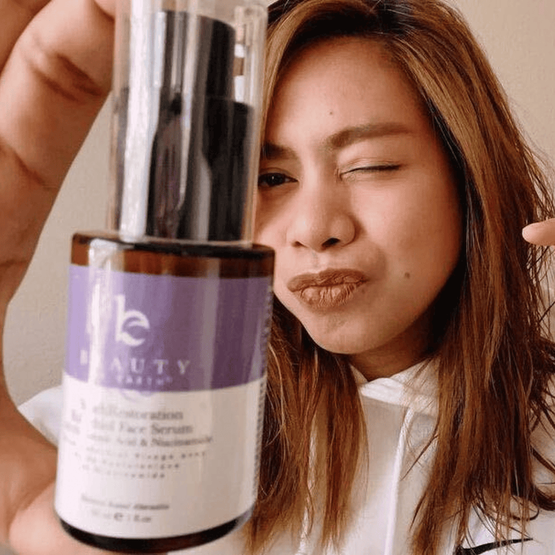 Person holding a bottle of 'The Beauty' serum close to their face