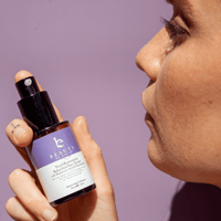 Person holding a bottle of 'Beauty' serum with a blurred background