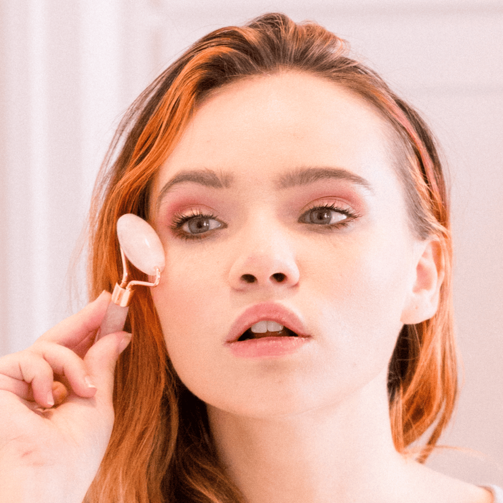 Woman applying cream to her face with a applicator against a neutral background