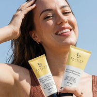 Woman holding two beauty by earth sunscreen products with a clear blue sky background