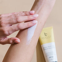 Person applying sunscreen to their arm with a tube of sunscreen visible.