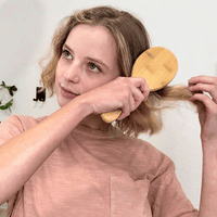 Woman brushing her hair with a wooden comb against a white background