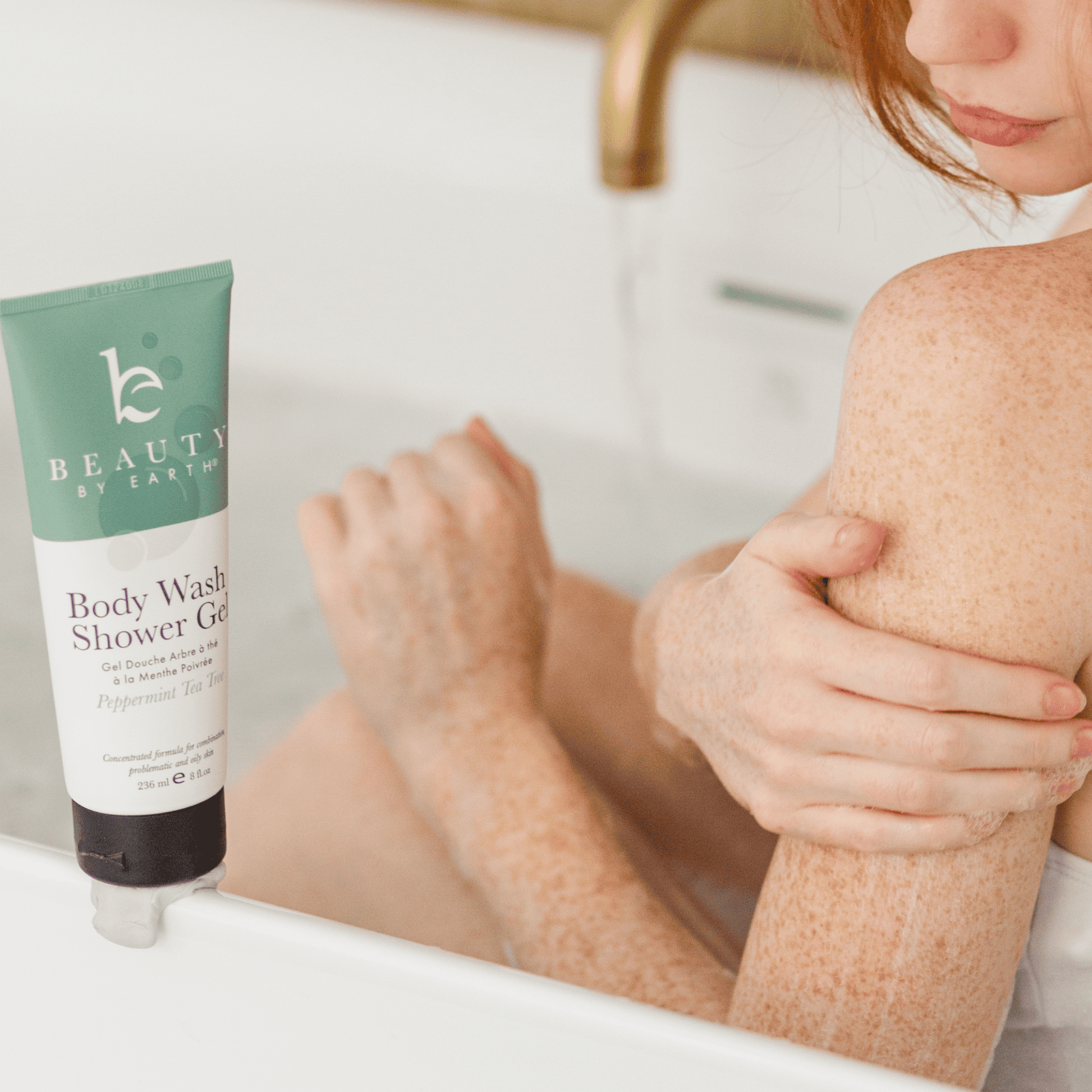 Person sitting in a bathtub with a bottle of 'Beauty by Shikha' body wash shower gel peppermint tea tree
