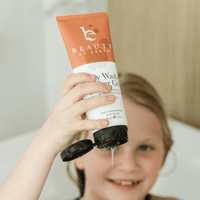 Child holding a tube of 'Beauty by Earth' body wash shower gel in vanilla coconut with visible brand name.