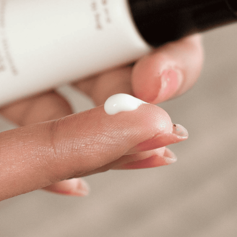 Close-up of a hand holding a small amount of coffee bean eye cream with a blurred background