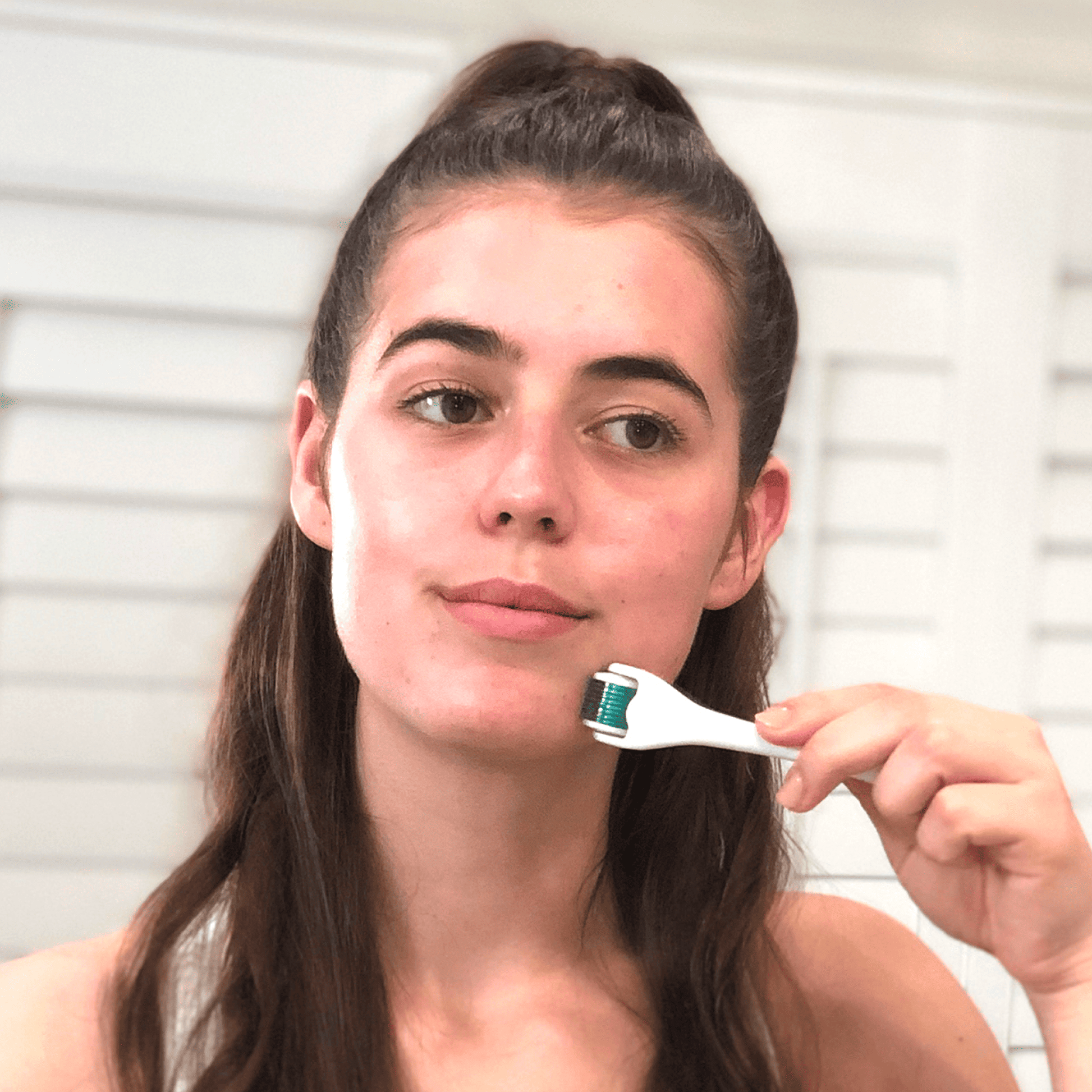 Woman holding a derma roller using it on her face with a neutral background