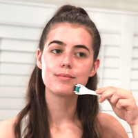 Woman holding a derma roller using it on her face with a neutral background