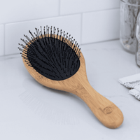 Wooden hairbrush with black bristles on a light gray surface.