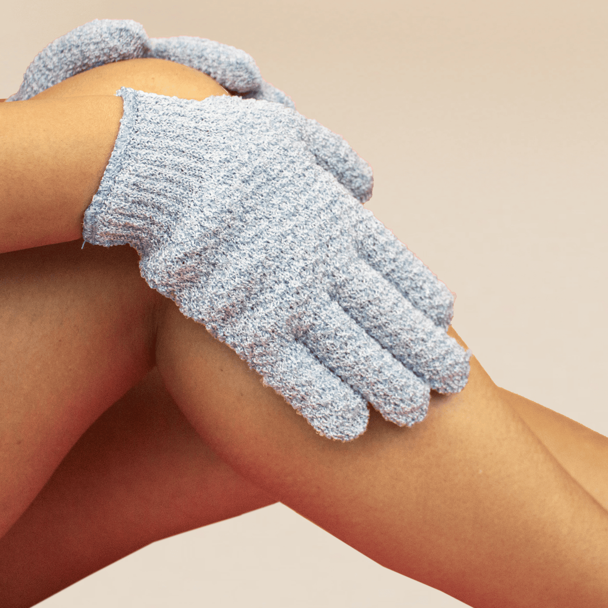 Heavy exfoliating gloves being worn on a person's hands against a beige background