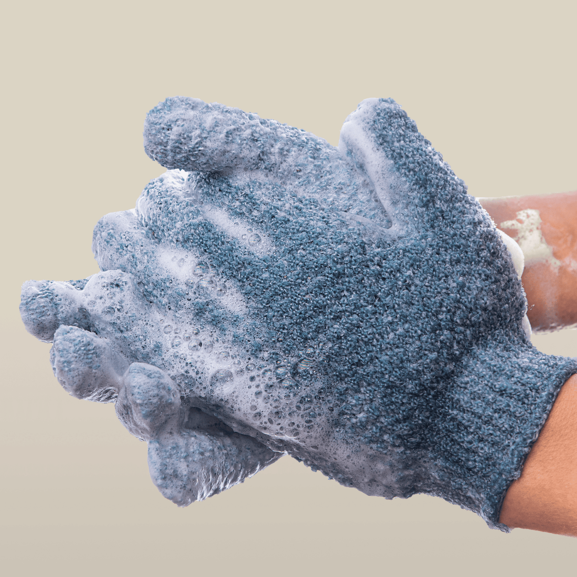 Heavy exfoliating gloves with soap suds on a beige background
