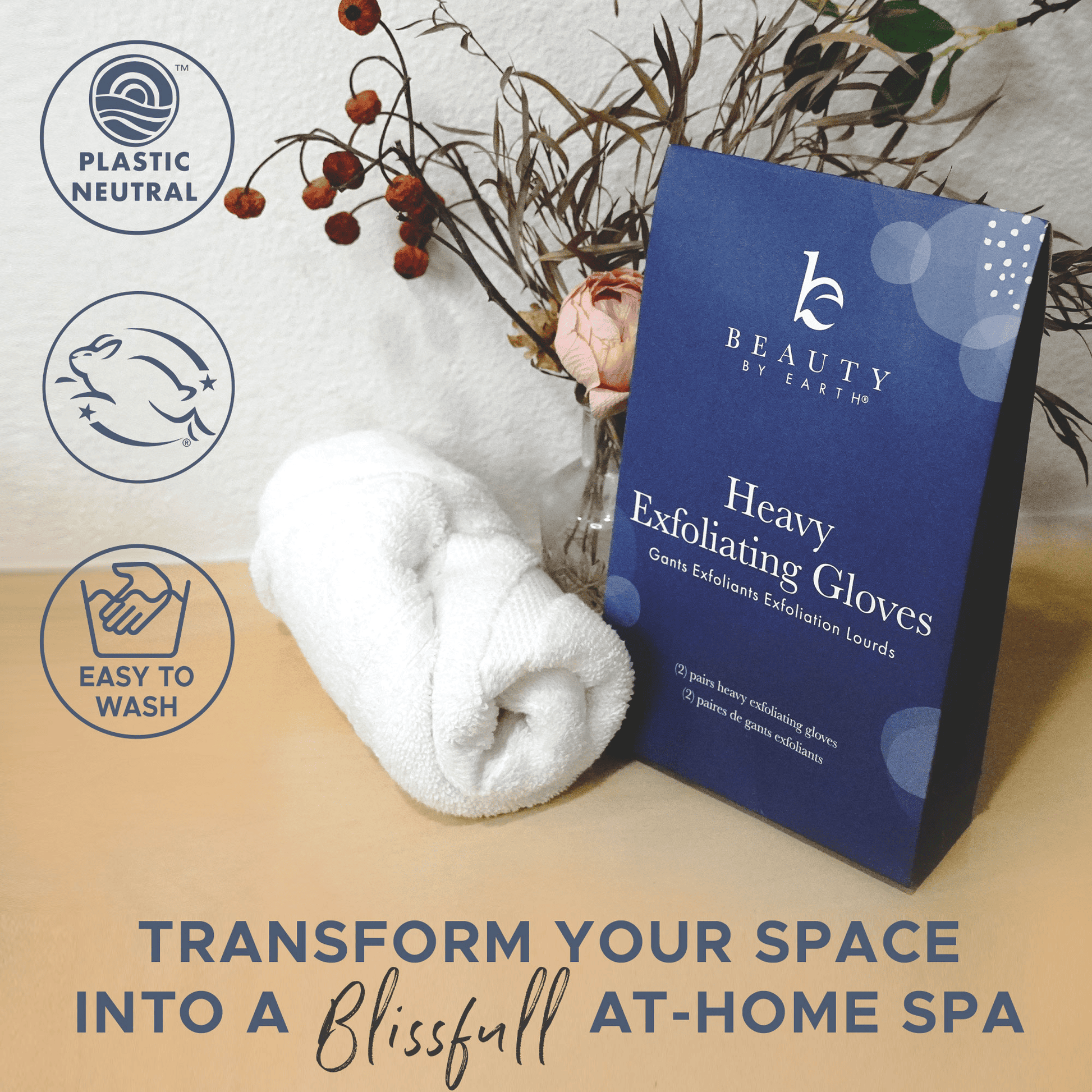 Blue box of 'Heavy Exfoliating Gloves' by Beauty by Earth with a towel and decorative elements on a neutral background.