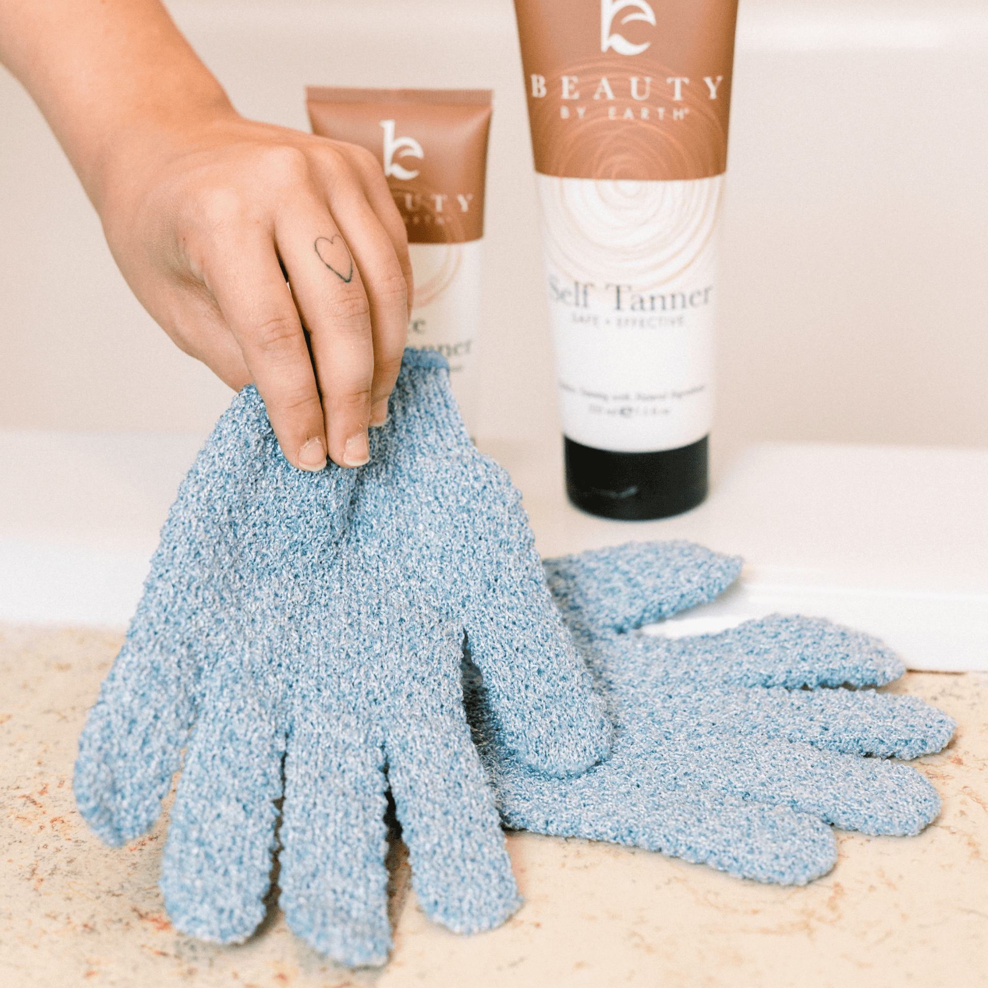 Heavy exfoliating gloves with a bottle of 'Beauty by Earth' self tanner in the background.